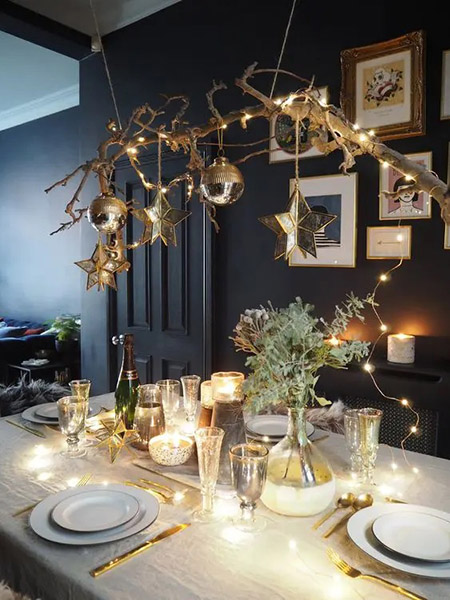 a chic Christmas tablescape with a branch with ornaments and stars hanging over the table lights